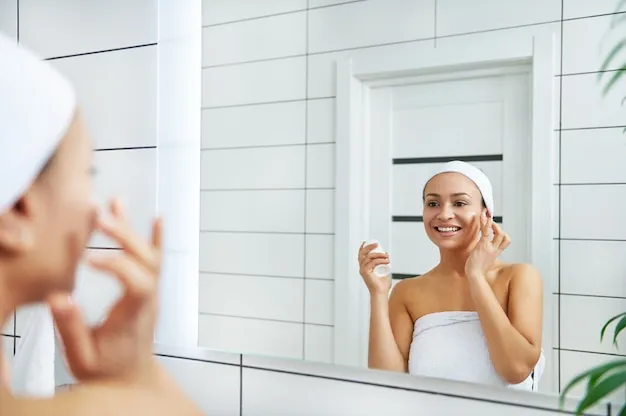 woman-applying-cream-face-with-finger-while-looking-her-reflection-bathroom-mirror_328764-792 Sử dụng đầu ngón tay giúp kem dưỡng có màu tiệp vào da tự nhiên nhất