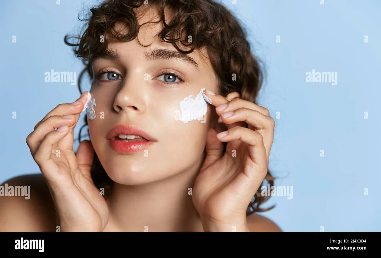 young-woman-looking-in-mirror-and-applying-facial-cream-on-her-cheeks-moisturizing-and-hydrating-skincare-product-on-clear-glowing-face-skin-2j4x3d4 Sự kết hợp đúng hoạt chất mang lại làn da khỏe mạnh và rạng rỡ